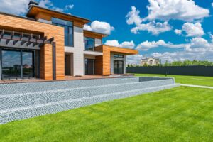 Exterior of contemporary residential house with panoramic windows glass doors and green lawn in yard on sunny day against blue sky with white clouds