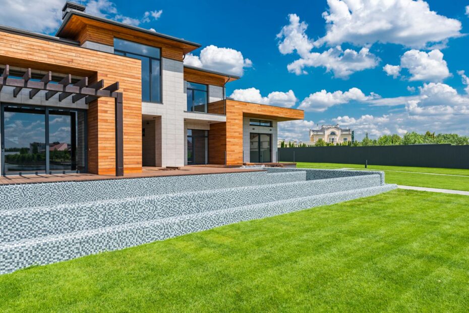 Exterior of contemporary residential house with panoramic windows glass doors and green lawn in yard on sunny day against blue sky with white clouds